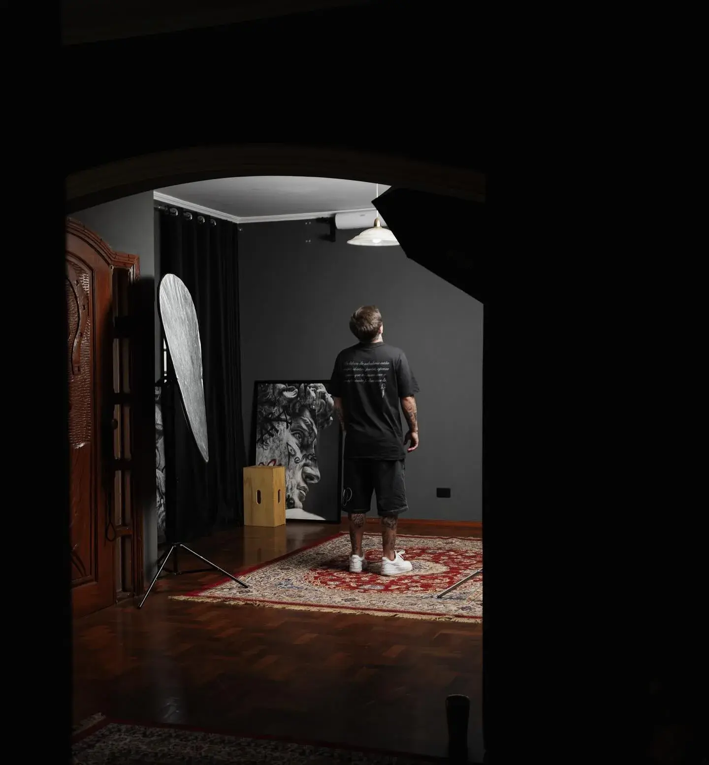 Gabriel Ferraciolli sentado no estúdio, iluminado por um softbox, entre telas e parede pintada