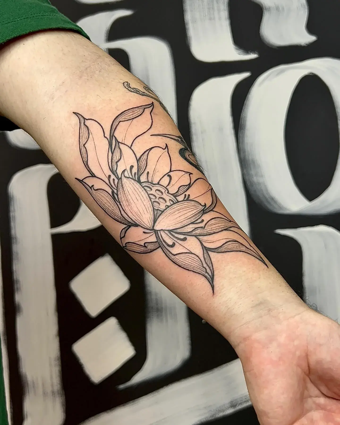 Flor de lótus em fine line no antebraço, parede de caligrafia ao fundo